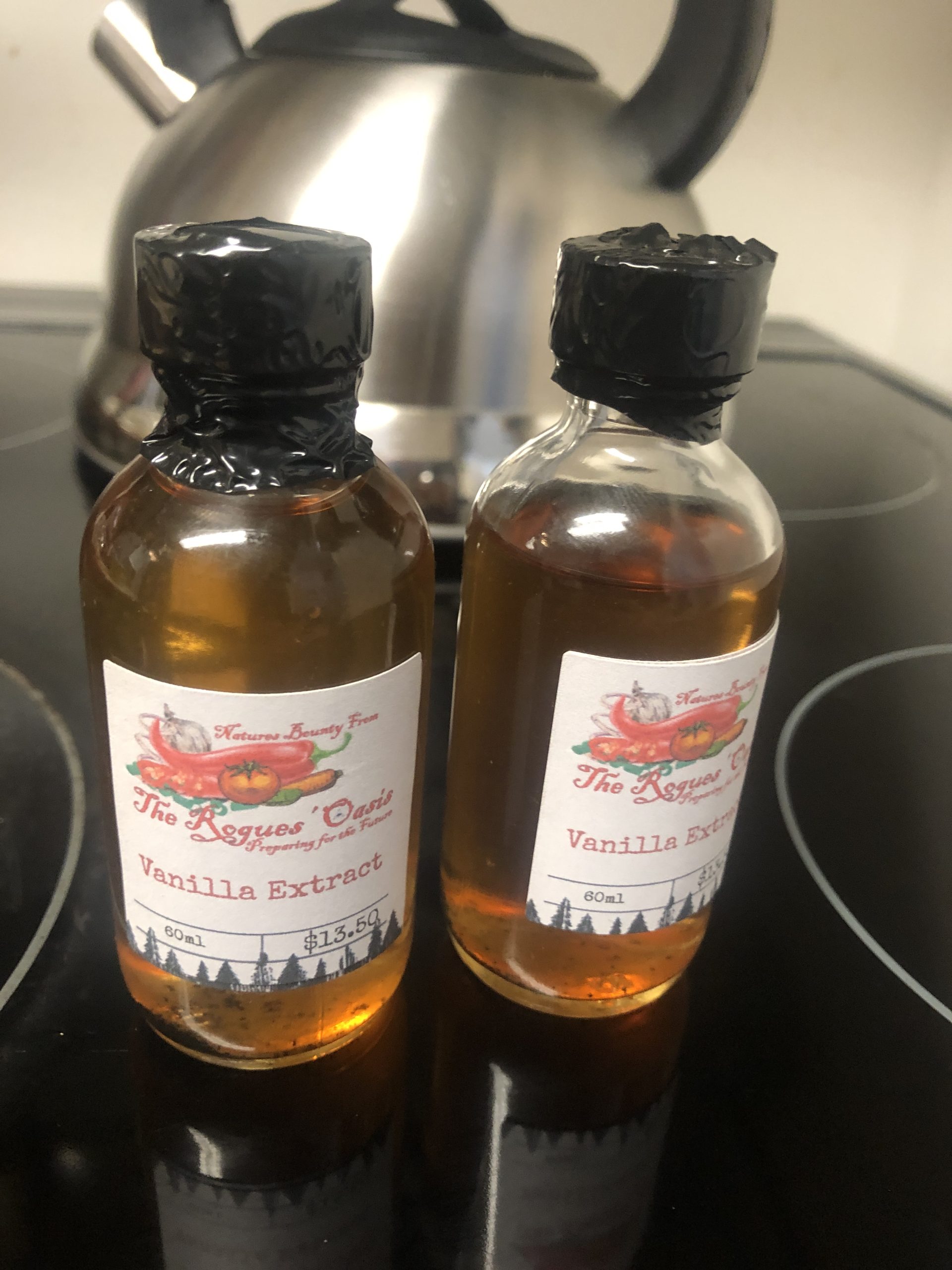 Two bottles of The Rogues' Oasis Vanilla Extract with black wax seals on a kitchen stove.