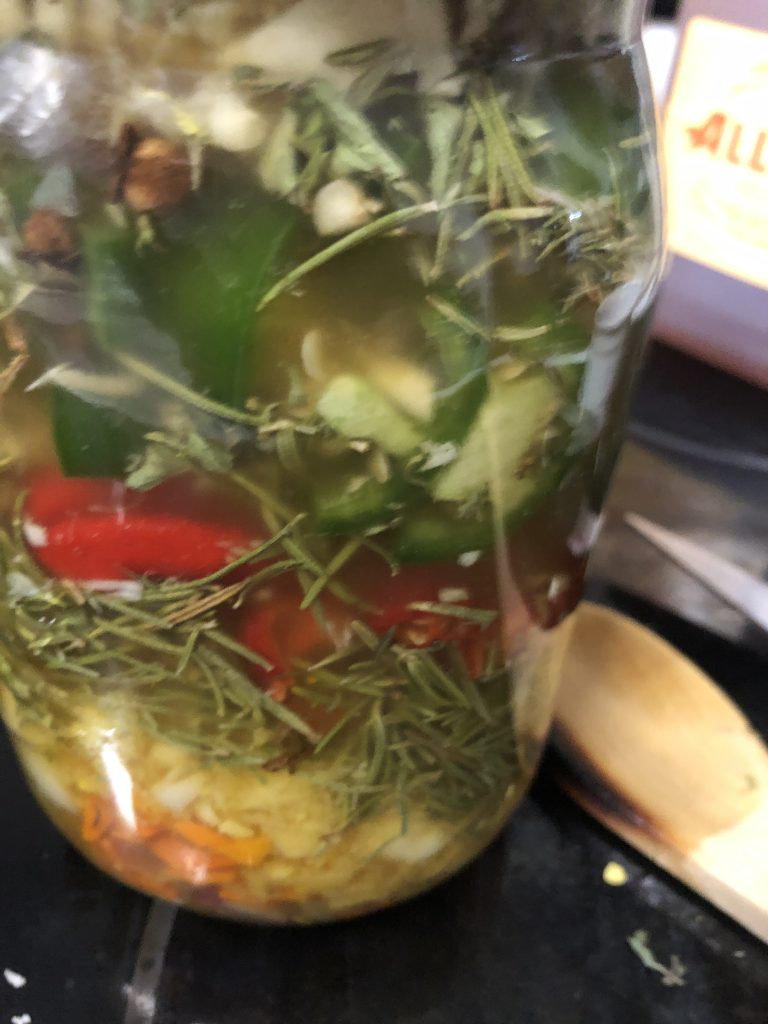 Jar of vibrant fire cider with colorful peppers and herbs.