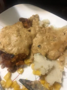 Savory dish with creamy sauce over crispy meat, served with fluffy mashed potatoes and bright yellow corn.