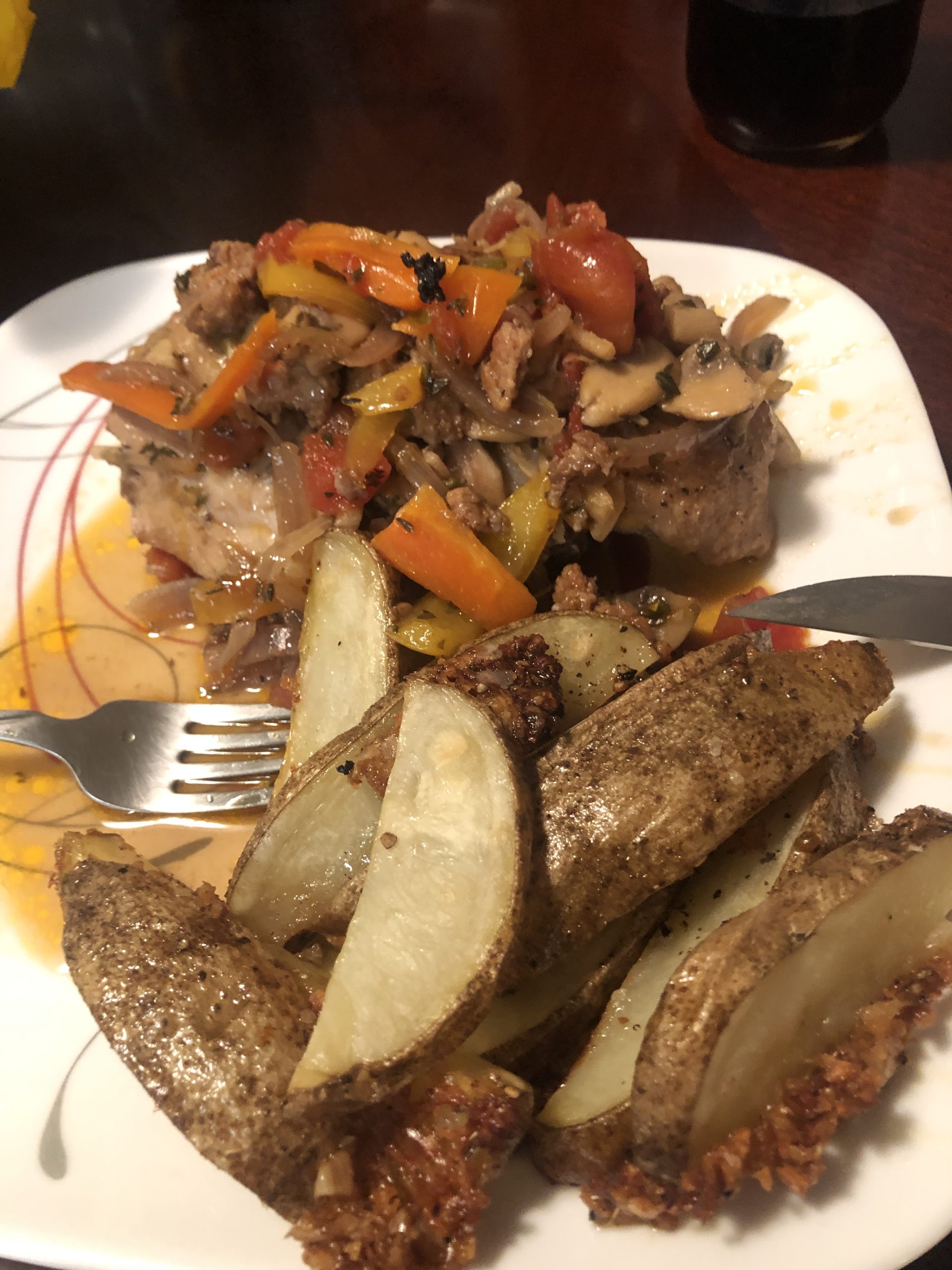Plate with savory meat topped with vibrant vegetables and crispy potato wedges.