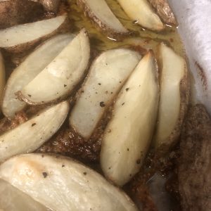 Golden potato wedges roasted to perfection, glistening with olive oil and a sprinkle of black pepper.
