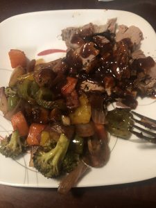 Savor the Rogue's rich beef slices drizzled with spicy sauce, flanked by vibrant roasted vegetables.