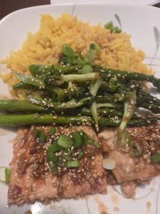 Delicious salmon topped with green onions and sesame seeds, alongside vibrant turmeric rice and sautéed broccolini.