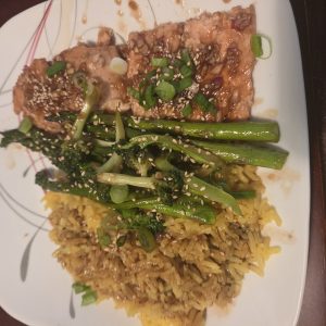 Delicious glazed salmon with sesame-topped broccolini and vibrant turmeric rice on a white plate.